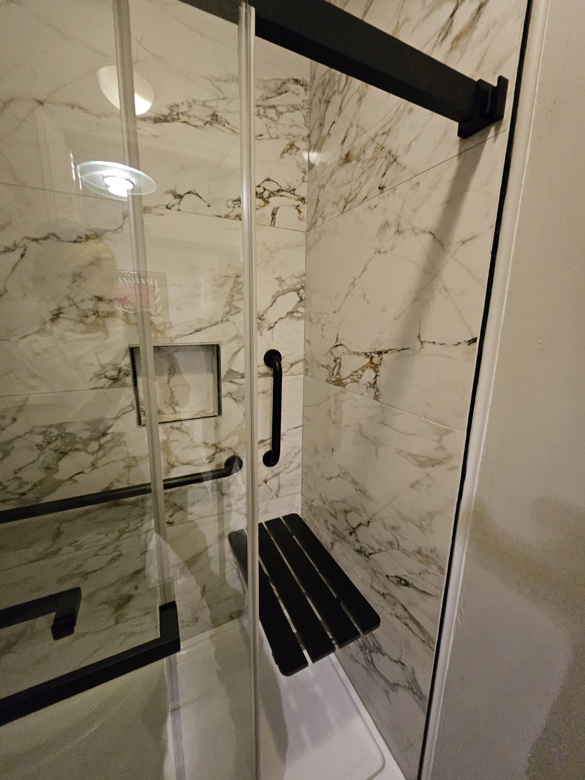 Close view of the finished shower tile, niche, grab bar, and fold-down seat
