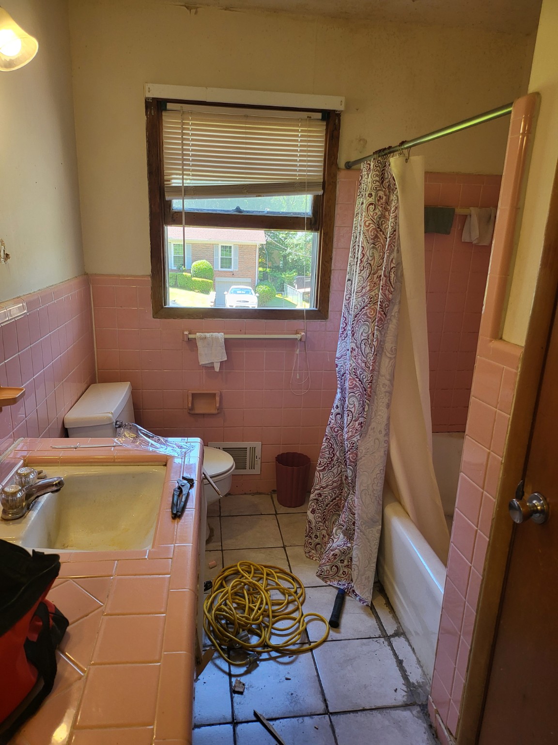 Bathroom before renovation with pink wall tile, an older vanity, and a shower curtain