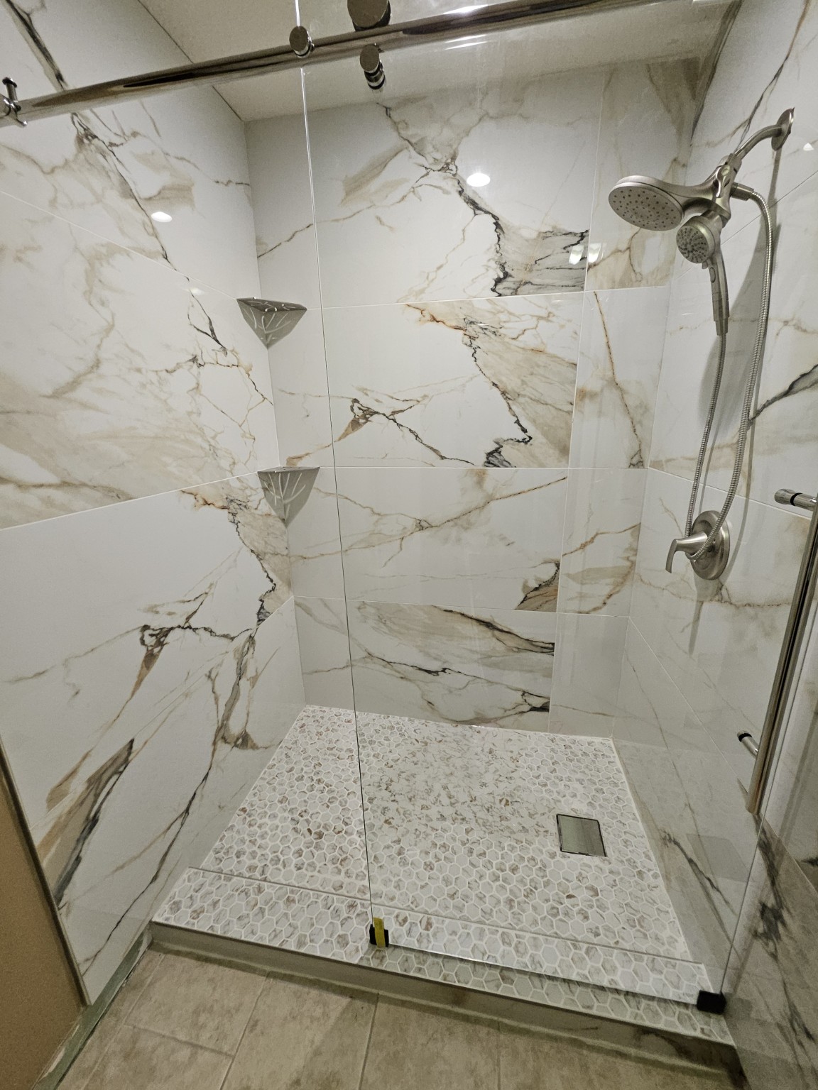 Same bathroom after renovation with a glass shower, marble-look tile, and mosaic floor
