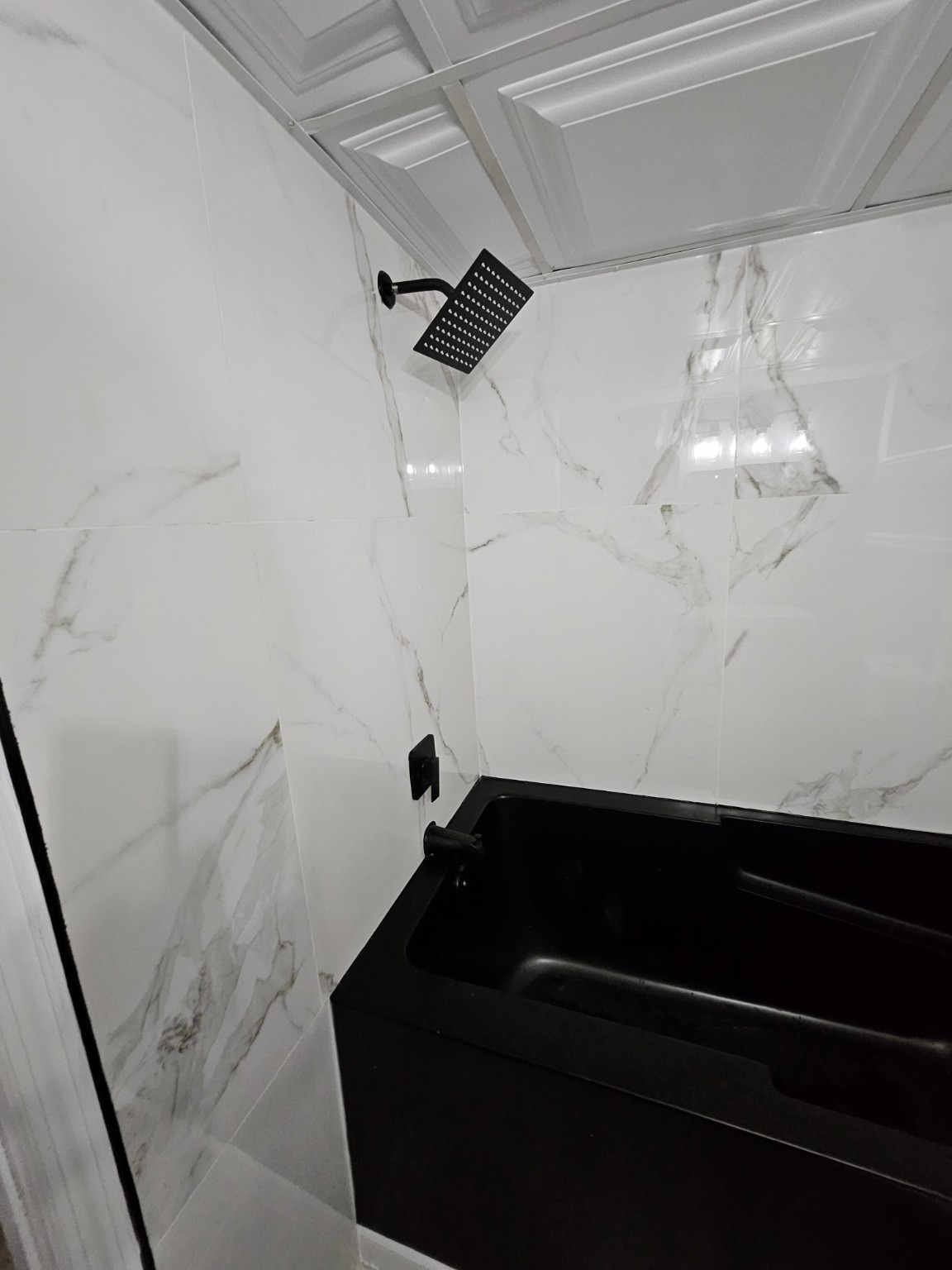 Finished bath with black shower fixture and marble-look tile