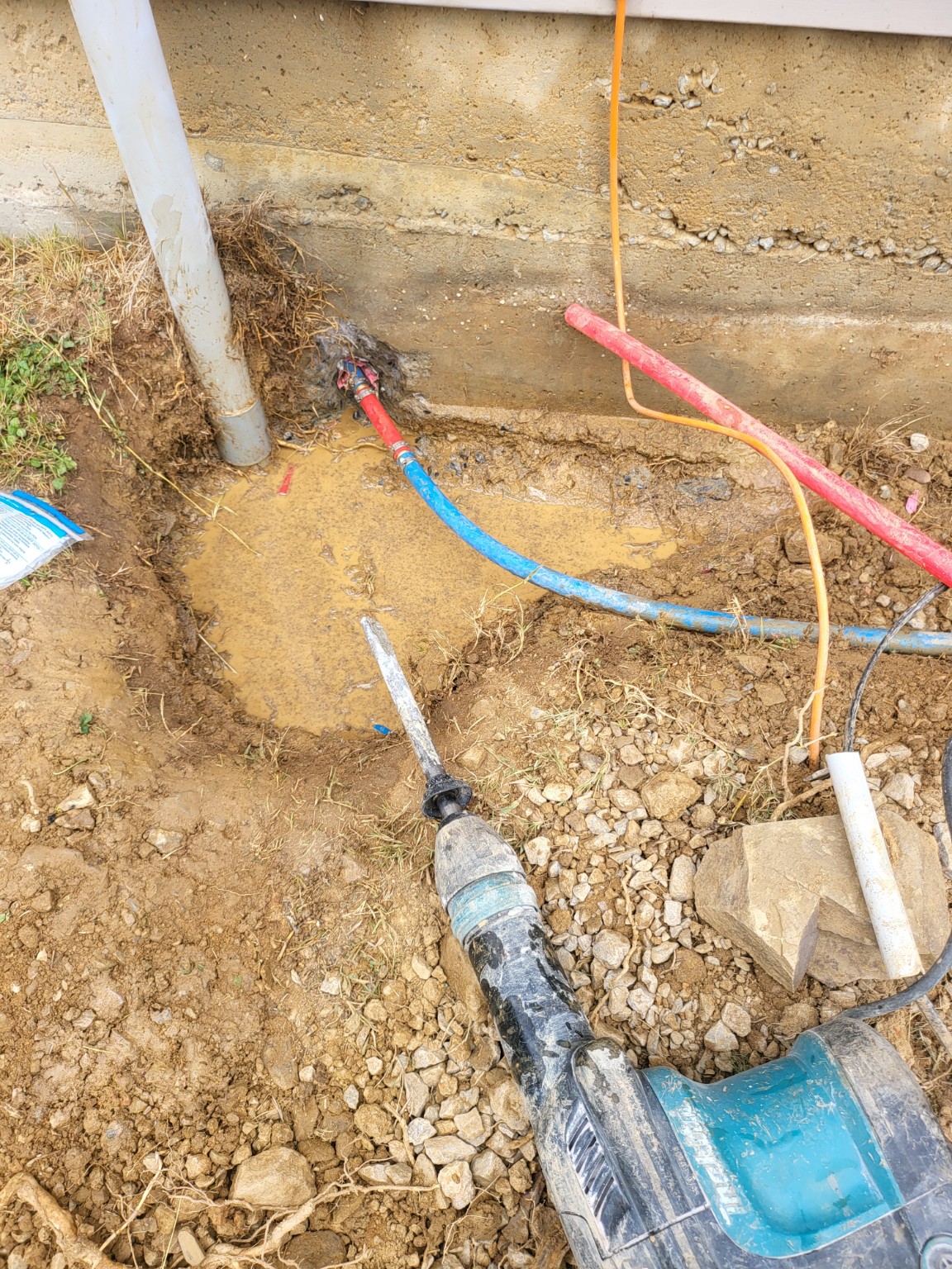 Excavated area with exposed red and blue plumbing lines alongside a foundation